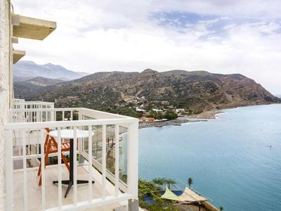 Balcone con sedia e tavolo su edificio bianco con vista sul mare e sulla costa rocciosa.