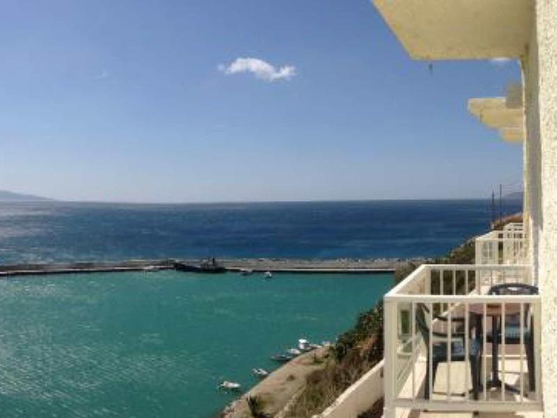 Balcone con tavolo e sedie con vista sul mare e cielo azzurro chiaro.