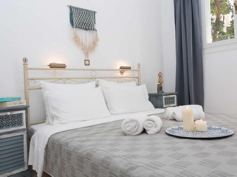 Camera luminosa con letto bianco, copriletto grigio, candele e asciugamani sul letto.