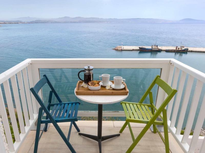 Balcone con sedie blu e verdi e servizio da caffè con vista sul mare.
