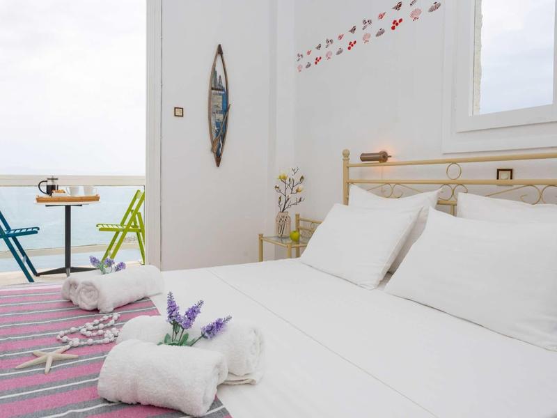 Camera moderna luminosa con vista mare, biancheria bianca e piccolo balcone con sedie.