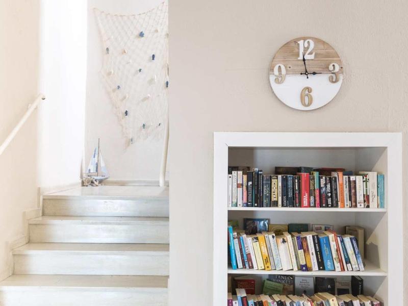 Scala luminosa con libreria e orologio da parete in un interno accogliente.