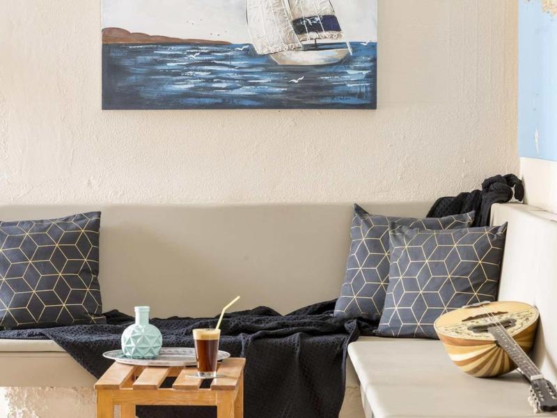 Angolo salotto accogliente con cuscini grigi, tavolino in legno e dipinto di barca a vela sul muro.
