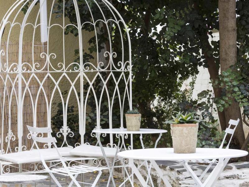 Tavolo e sedie in metallo bianco sotto un albero accanto a una struttura metallica bianca decorativa.