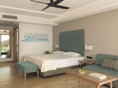 Camera d'hotel moderna con letto matrimoniale, divano, pavimento in legno e vista sul corridoio.