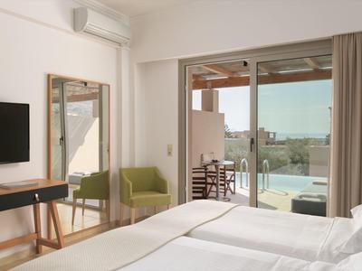 Camera d'hotel moderna con letto matrimoniale, poltrona verde e vista su terrazza con piscina.