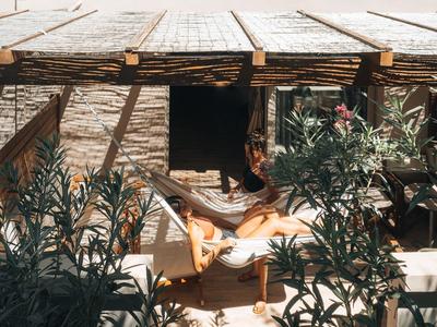 Donna rilassata su una poltrona sotto un pergolato in legno, circondata da vegetazione.