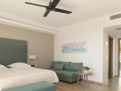 Camera d'hotel con letto matrimoniale, divano grigio, tavolino rotondo e ventilatore a soffitto.