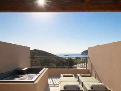 Terrazza con vasca idromassaggio e lettini con vista sul mare e sulle colline sotto un cielo sereno.