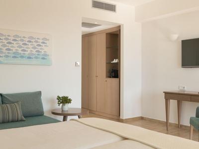 Camera d'hotel luminosa con divano, letto, tavolino, TV e arredi semplici.