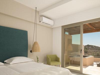 Camera d'hotel luminosa con letto matrimoniale, poltrona verde e accesso a una terrazza con vista montagna.