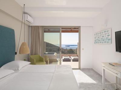 Camera d'hotel luminosa con letto matrimoniale, poltrona, balcone e vista mare.