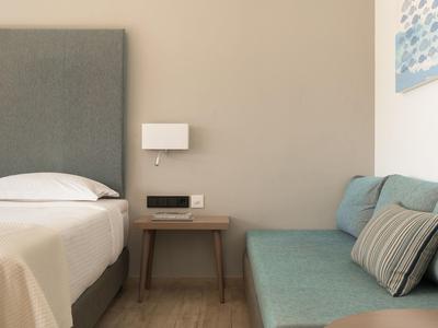 Camera d'hotel con letto grigio, tavolino in legno e divano azzurro chiaro.