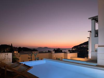 Piscina moderna illuminata al crepuscolo con vista sul mare e le montagne.