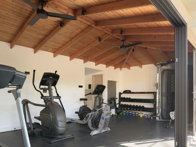 Palestra con macchine per esercizi e rastrelliera per manubri sotto un soffitto in legno.