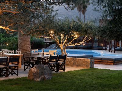 Terrazza con tavoli e alberi illuminati vicino a piscina di sera.