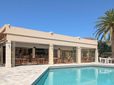 Piscina davanti a un edificio moderno con terrazza e palme sotto un cielo azzurro.