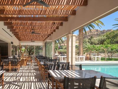 Terrazza ombreggiata di un ristorante con piscina e paesaggio verde.