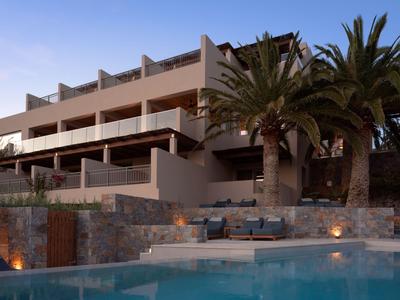 Hotel moderno su più piani con terrazza illuminata e piscina al crepuscolo.