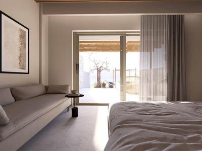 Camera d'hotel moderna con letto, divano grigio, TV e terrazza esterna luminosa.