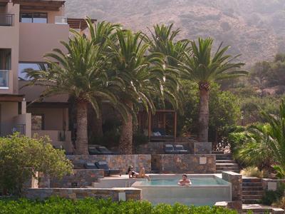 Hotel con piscina e palme davanti a uno sfondo montuoso in una giornata di sole.