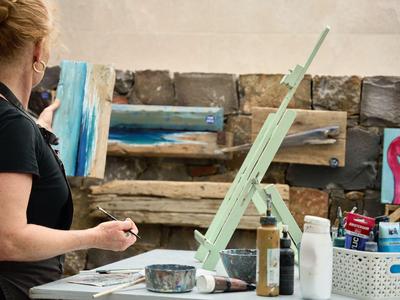 Artista che dipinge su un cavalletto in uno studio con barattoli di vernice e pennelli.