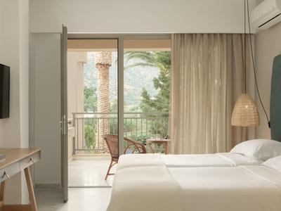 Camera d'hotel luminosa con letto matrimoniale e balcone con vista verde.