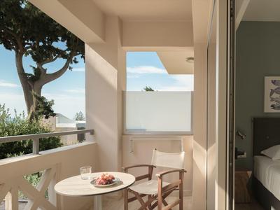 Balcone dell'hotel con piccolo tavolo rotondo, due sedie, vista su alberi e cielo.