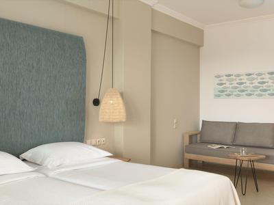 Camera d'hotel moderna con letto matrimoniale, divano grigio e arredamento minimalista.