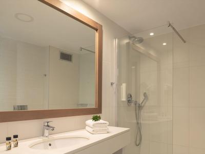 Bagno moderno con grande specchio, lavabo, asciugamani e doccia a vista in toni soft.