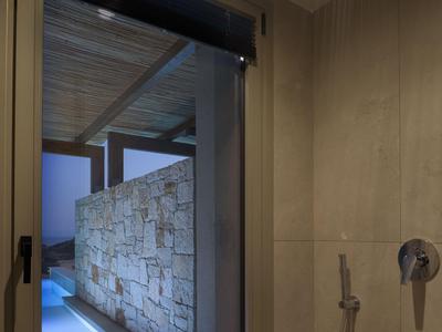 Blick von einem hell beleuchteten Badezimmer durch eine offene Tür auf einen beleuchteten Außenpool und eine Steinmauer.