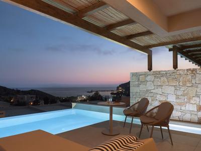 Luxuriöse Terrasse mit Pool, Stühlen und Blick auf das Meer bei Sonnenuntergang.