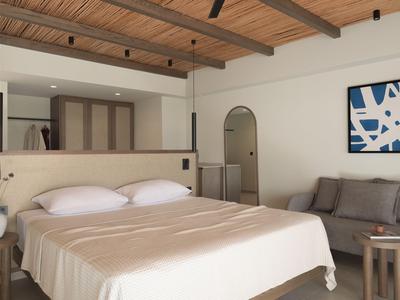 Camera d'hotel luminosa con letto matrimoniale, divano grigio, soffitto in legno e quadro astratto.