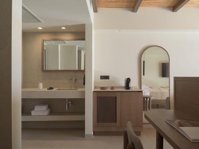 Area moderna della camera d'hotel con lavabo, specchio, soffitto in legno e vista parziale di un tavolo.