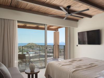 Camera d'hotel moderna con letto e balcone con vista sul mare e una collina boschiva.