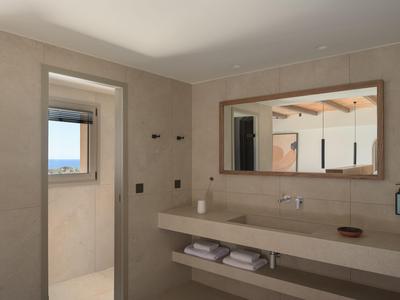 Bagno moderno con grande specchio, lavandino e porta aperta che mostra una finestra con vista.