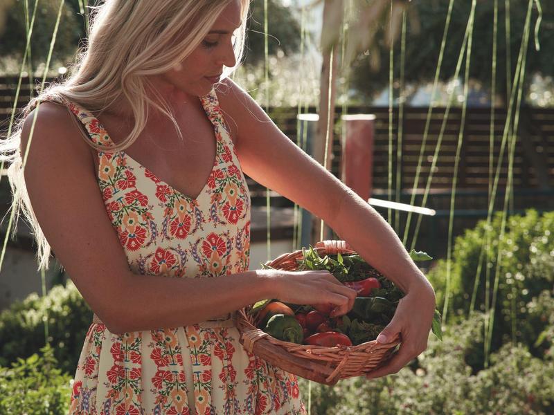 Giovane donna che raccoglie verdure in un giardino rigoglioso.
