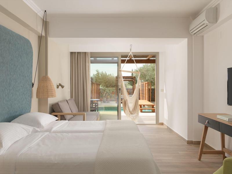 Camera d'hotel luminosa con letto matrimoniale, balcone e sedia sospesa per relax.