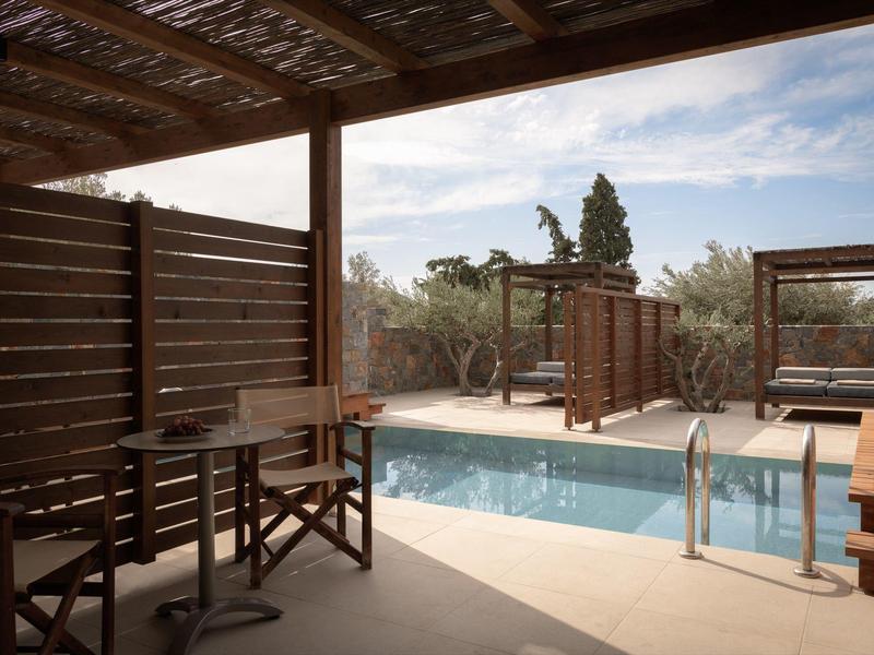Terrazza ombreggiata con tavoli, sedie e piscina all'aperto circondata dalla natura.