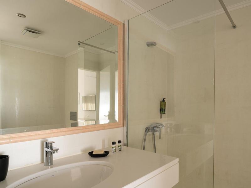 Bagno luminoso con lavabo bianco, specchio e cabina doccia in vetro.