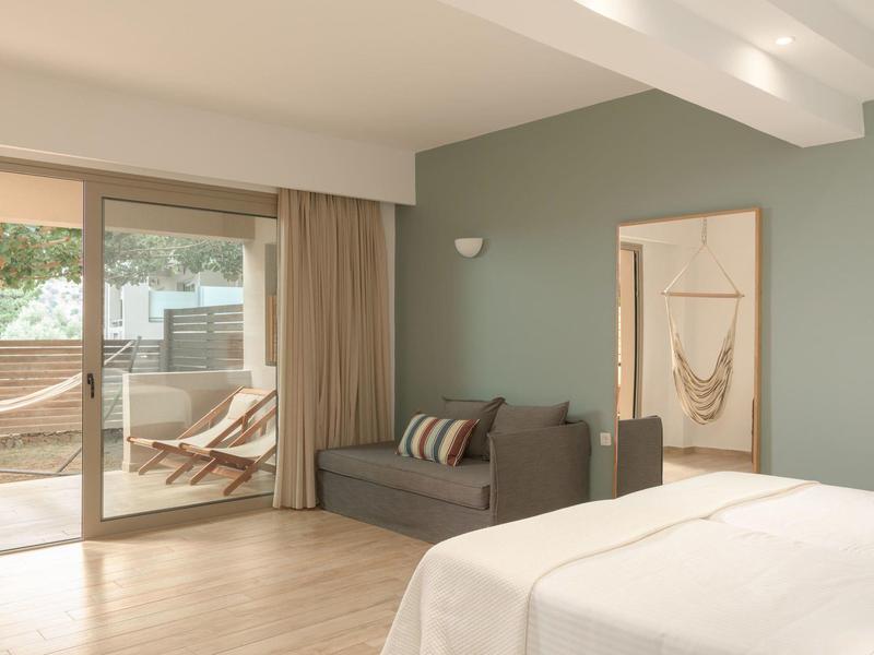 Camera d'hotel luminosa con letto, divano, terrazza e amaca esterna.