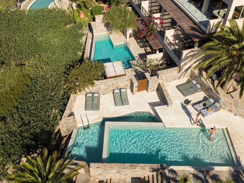 Piscina esterna con lettini, vegetazione e edificio moderno.