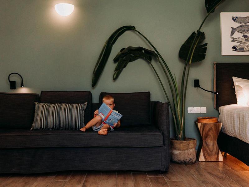 Bambino seduto su un divano nero in una stanza con pianta e letto.