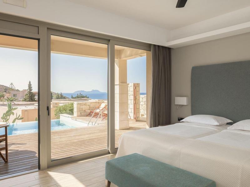 Camera d'hotel luminosa con letto matrimoniale e vista su terrazza con piscina e mare.