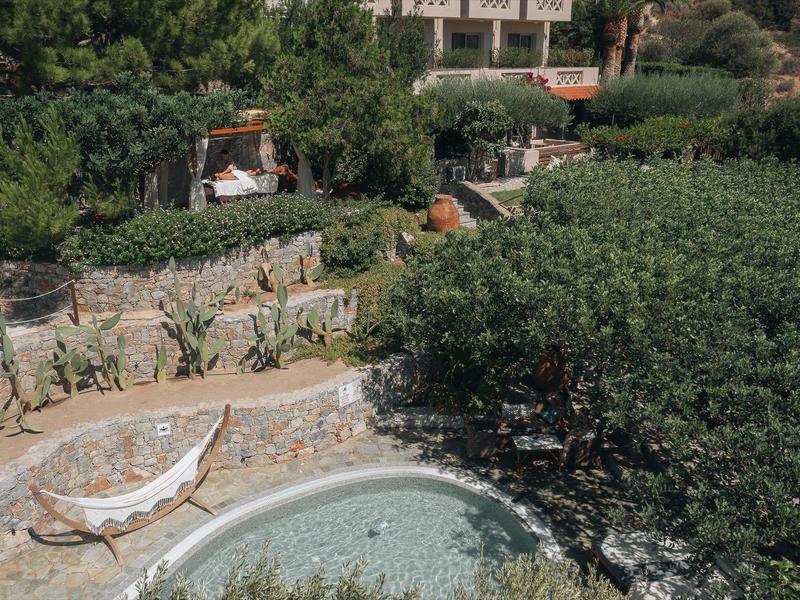 Piscina rotonda circondata da pietre con sdraio in un giardino verde.