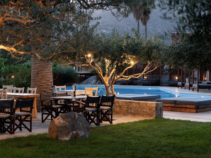 Terrazza con tavoli e alberi illuminati vicino a piscina di sera.