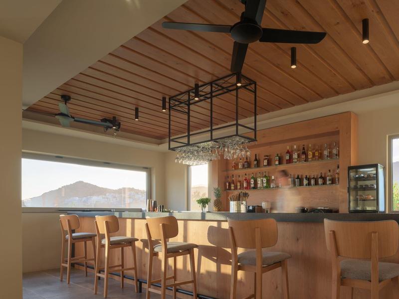 Bar moderno con sgabelli in legno, grande finestra e soffitto in legno con ventilatore.