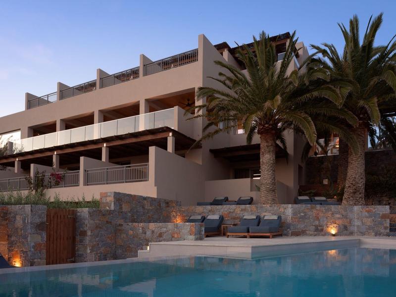 Hotel moderno con piscina, terrazza in pietra e palme al tramonto.