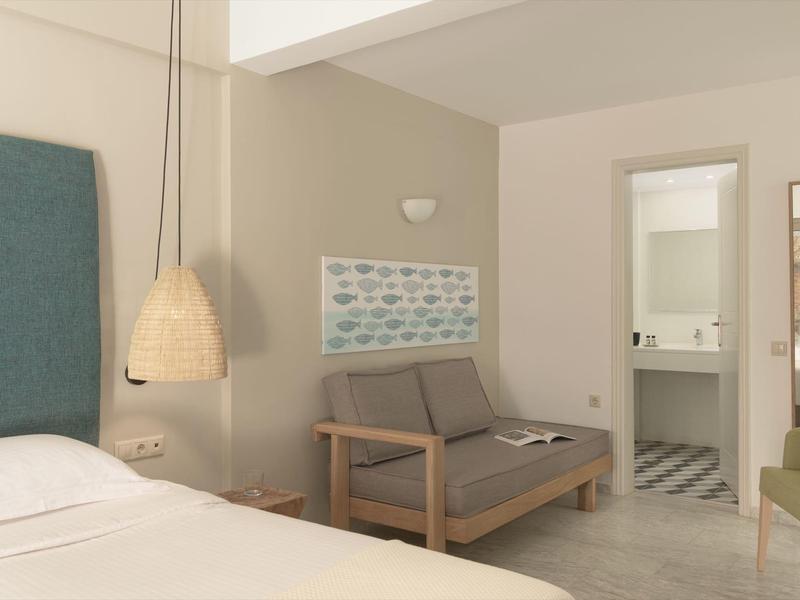 Camera d'albergo luminosa con letto bianco, divano grigio e decorazioni azzurre.