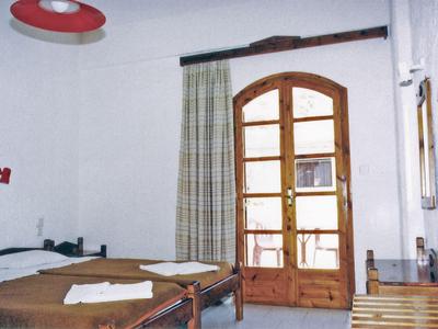 A simple hotel room with two beds, wooden doors, and a window with curtains.